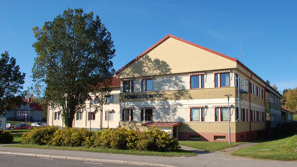 Tegel- och träbyggnad bakom en häck med ölandstok. Kommunhuset i Bergsjö.