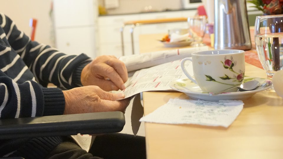 En gammal man sitter och läser och dricker kaffe.