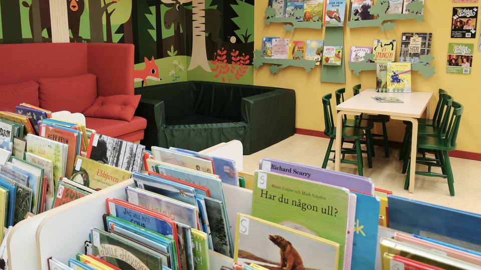 Barnhörna på biblioteket med böcker, soffa, bord och stolar.